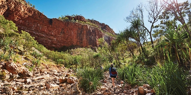 woman with backpack walking uphill towards red rockface