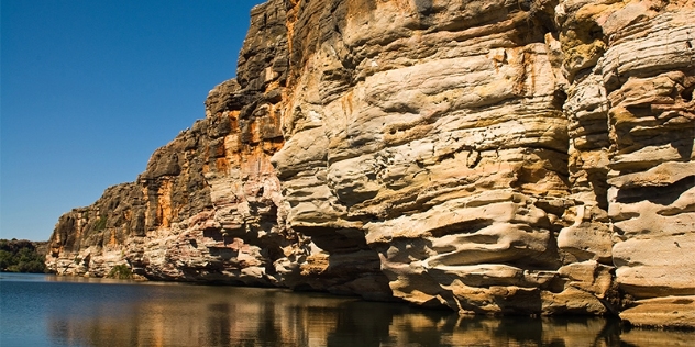 water level view of ocre patterned rockface overhanging the water