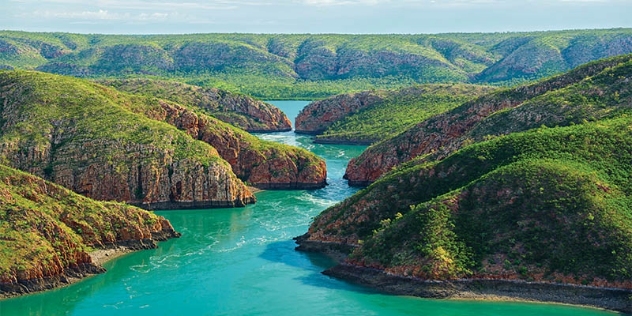 arial view of turquoise waters and white foam and green covered hills